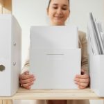 Personne assise a un bureau qui trie des documents administratifs dans des pochettes et classeurs
